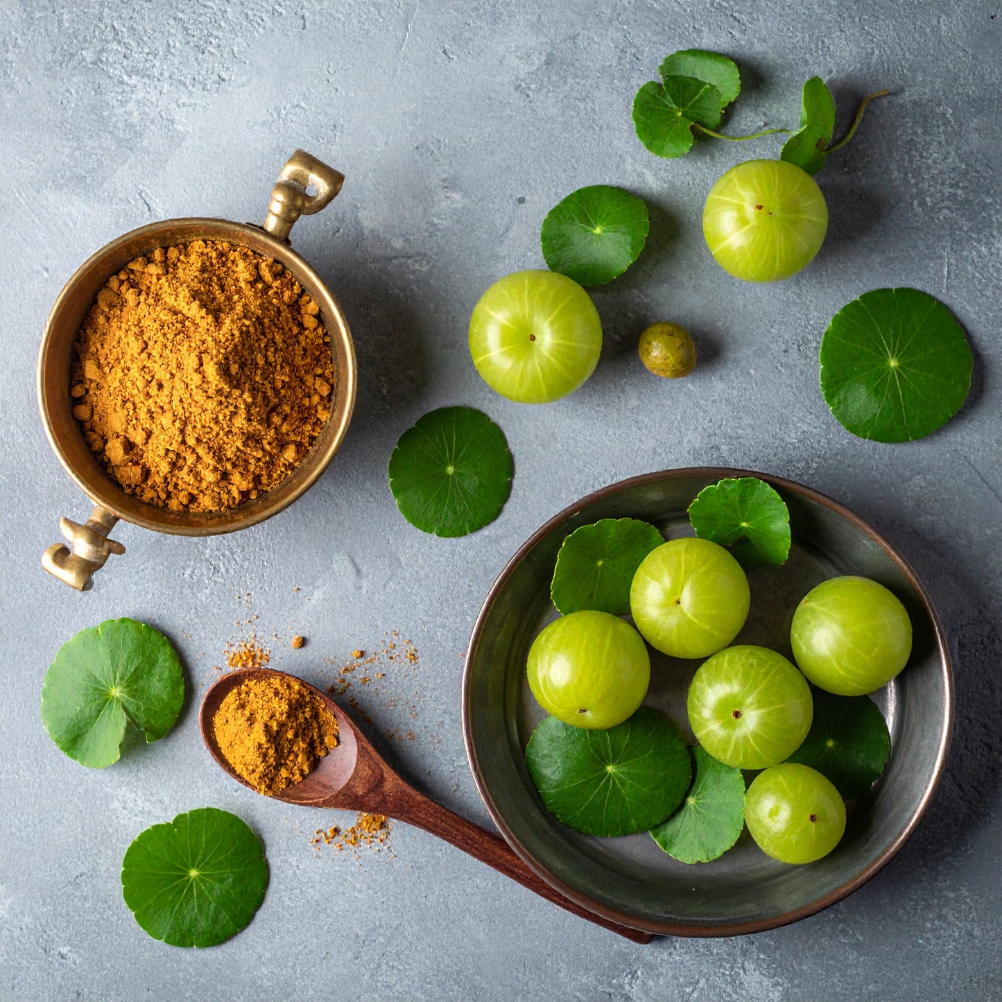 Amla e centella asiatica accanto a una ciotola di rame con polvere vegetale.